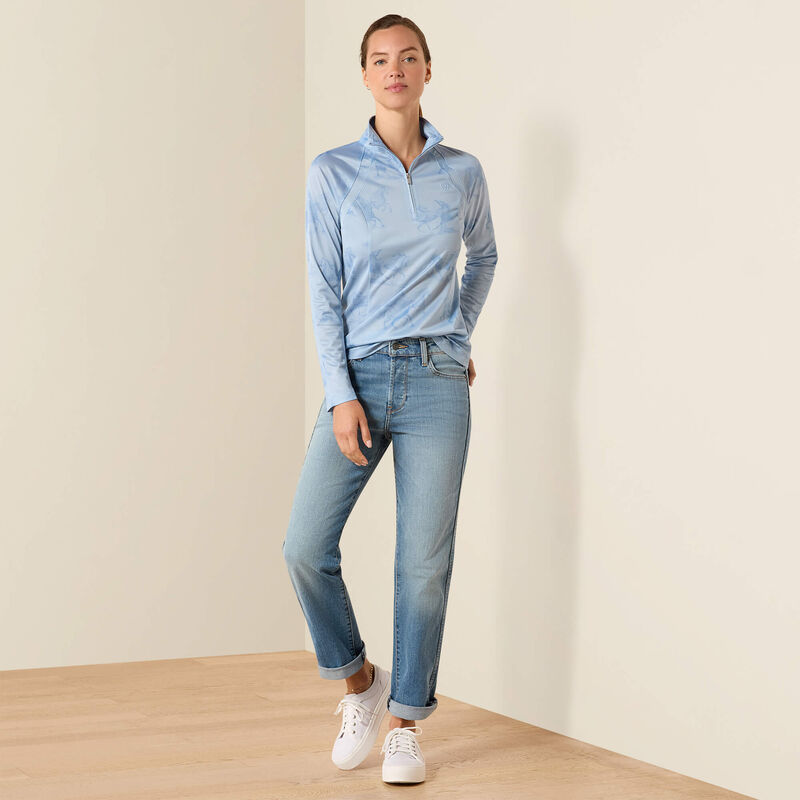 Person wearing a light blue long-sleeve shirt and jeans standing against a plain background