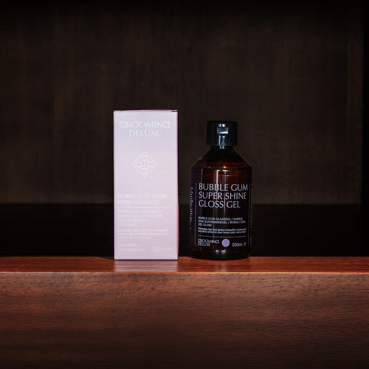 Bottle of 'Bubble Gum Super Shine Glossigel' and its packaging on a wooden surface with a dark background.