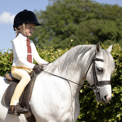 Child riding a white horse with greenery in the background