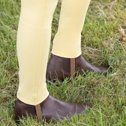 Brown riding boots and yellow pants on a grassy background