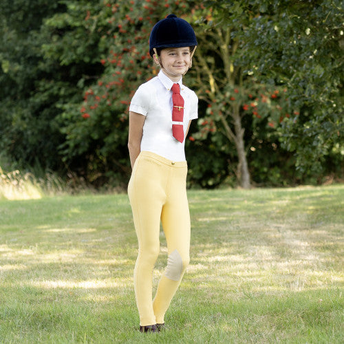 Person in equestrian attire with yellow pants and a red tie standing in a grassy area.