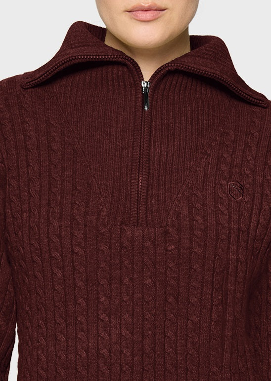 A close-up of a person wearing a ribbed, cable-knit half-zip sweater in a deep burgundy or maroon color, featuring a small embroidered logo on the chest.