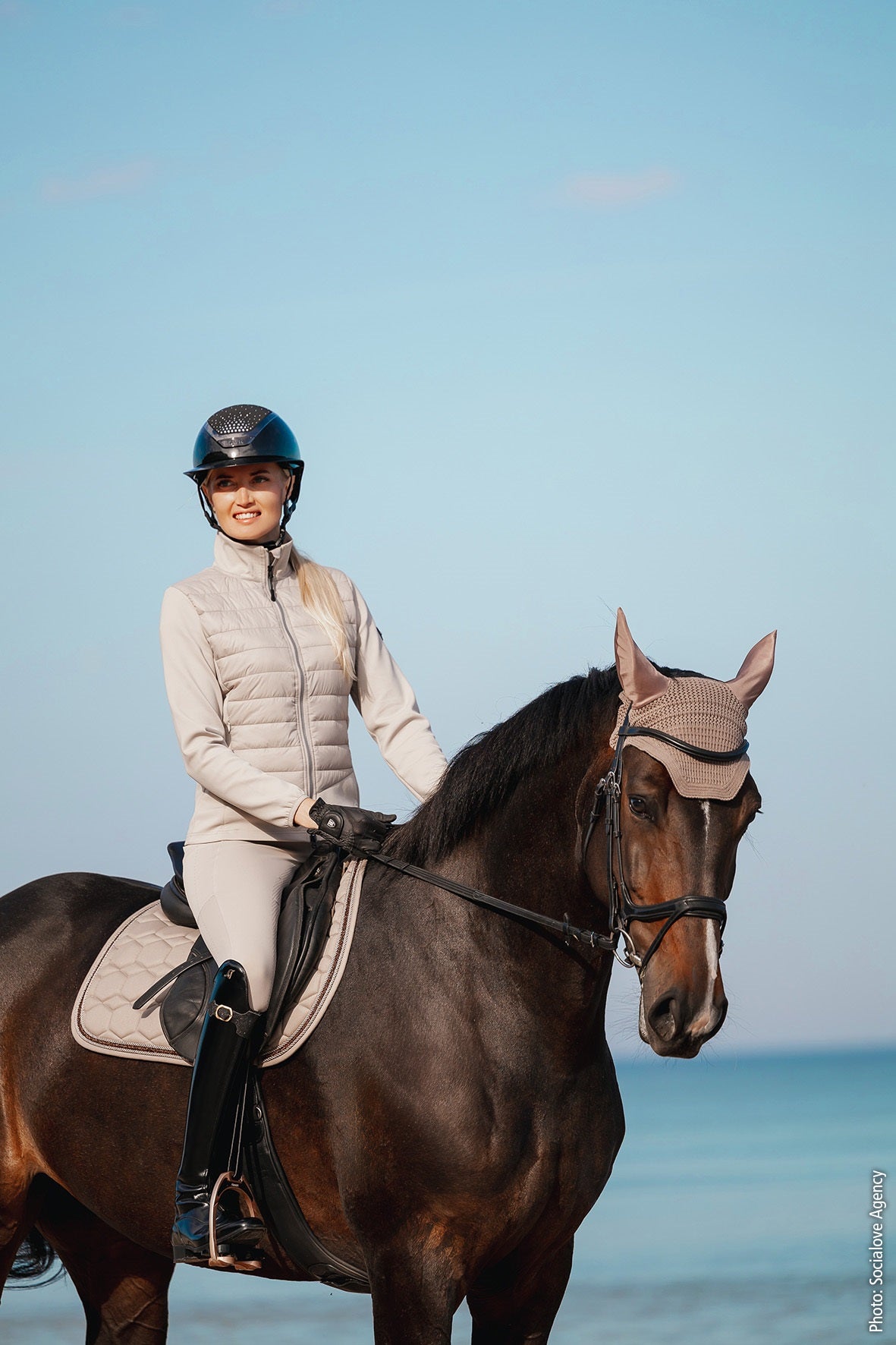 Woman riding a horse on a beach with clear blue sky