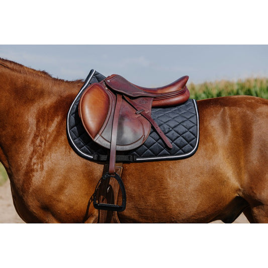 Brown horse with a leather saddle and black quilted saddle pad on a blurred natural background
