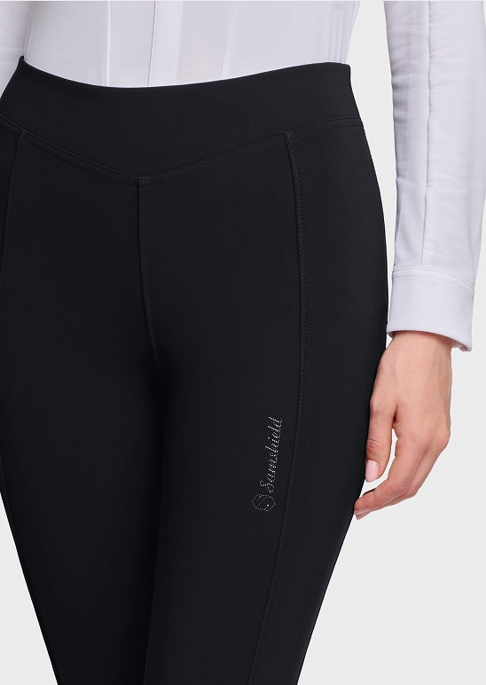 Black riding tights with a subtle vertical logo on the lower left leg, worn by a model in a white long-sleeve shirt against a light gray background.