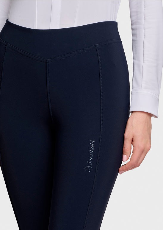 Close-up of a person wearing dark navy equestrian leggings with a white long-sleeve shirt, showing the side seam and a small white 'Simsolid' logo on the thigh.