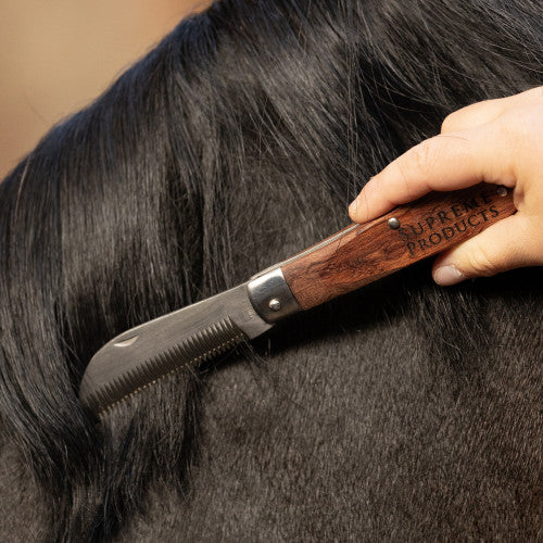 Person holding a mane thinning knife on the end of a brown horses' mane