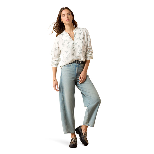 Woman wearing a white blouse with floral patterns and light blue jeans on a white background