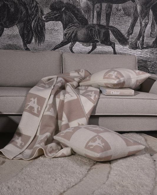 Throw and cushion and a book on a beige sofa with horse wallpaper behind