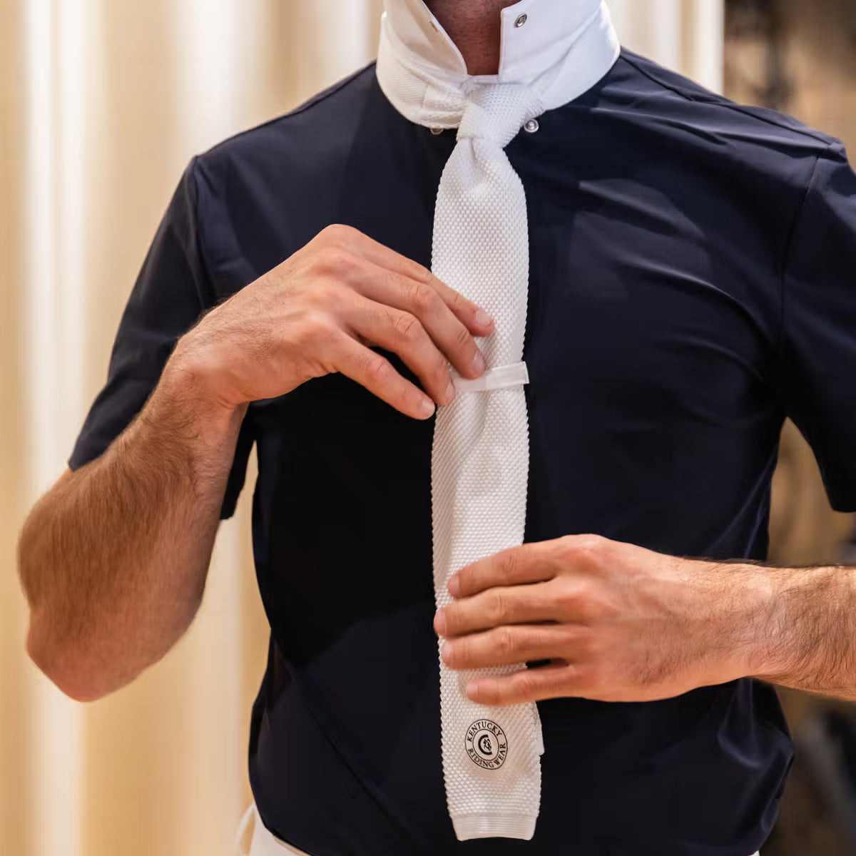 Person adjusting a white tie on a black shirt with a blurred background