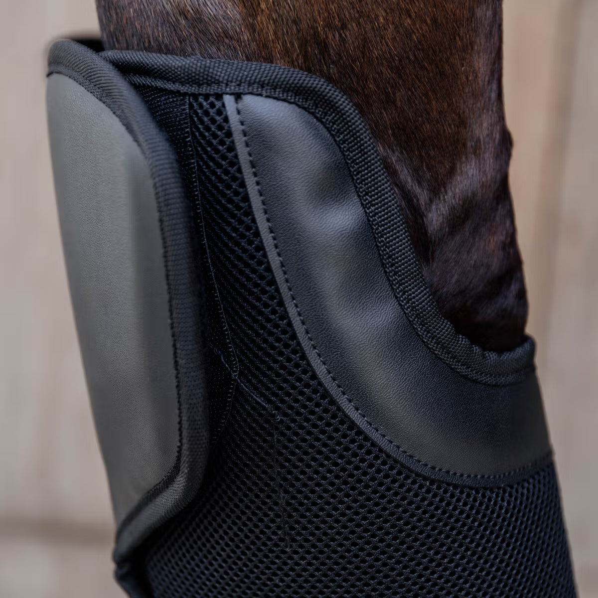 Black protective boot on a horse's leg with a neutral background