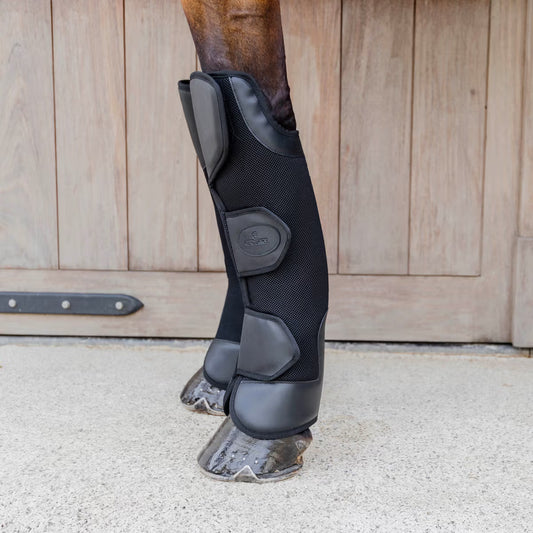Black protective leg wraps on a horse's leg with a wooden stable door in the background.