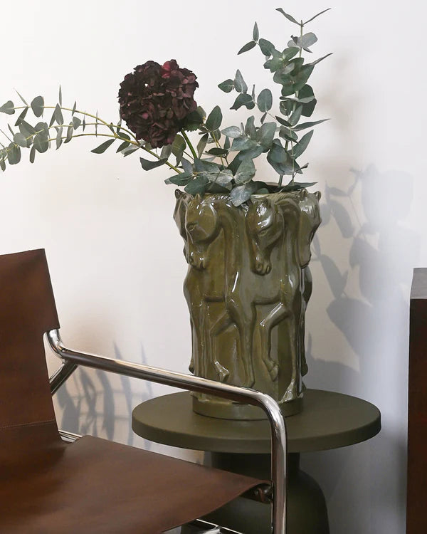 A green horse themed vase with flowers in it in a home setting