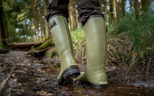 Person wearing green rubber boots walking through a forest