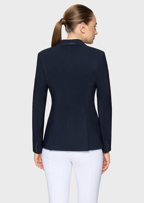 A woman shown from the back wearing a dark navy equestrian-style blazer and white pants against a light gray studio background.