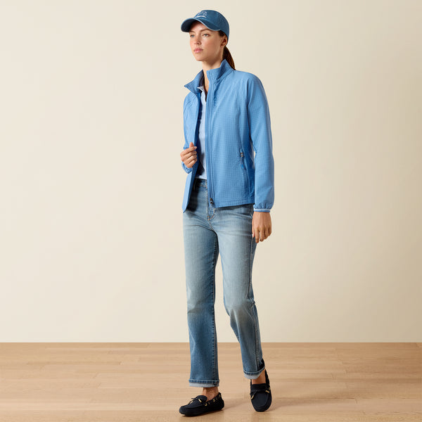 Person wearing a blue jacket and jeans standing on a wooden floor with a beige wall background