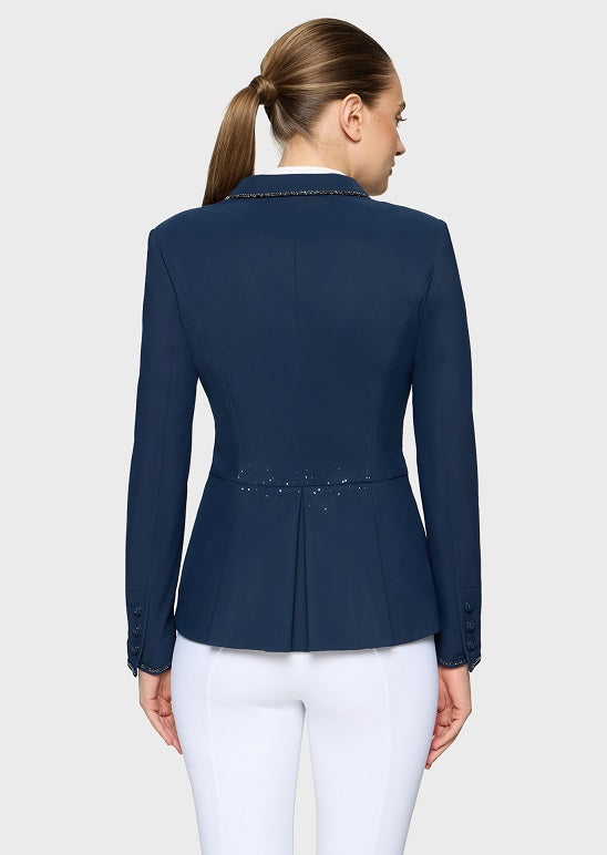 A woman shown from the back wearing a navy blue equestrian-style blazer with decorative gold embroidery on the collar and waist, paired with white riding pants, against a light gray studio background.