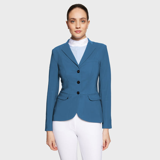 Woman wearing a blue competition jacket over a light blue shirt and white pants on a white background