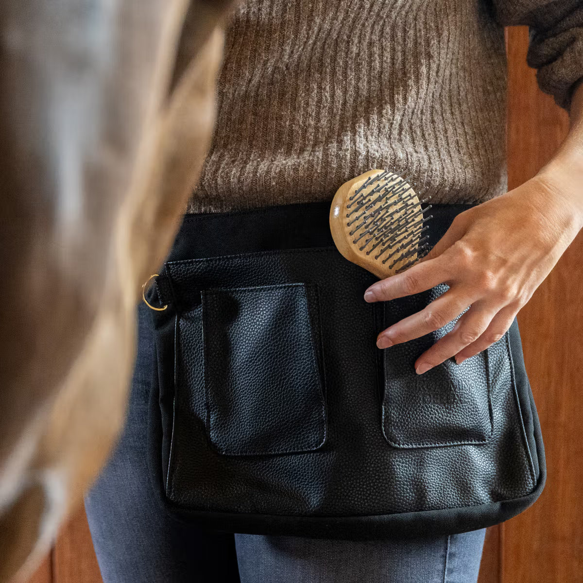 Person holding a black leather bag with a horse in the background