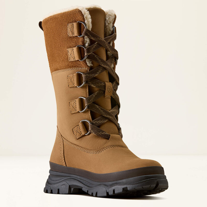 A tall tan winter boot with dark brown laces, silver metal eyelets, and a black rugged sole, shown against a plain off-white background.