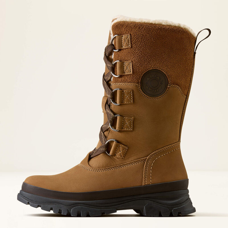 A brown suede and leather lace-up winter boot with a black sole, brown laces, and a white faux-fur lining, shown in profile against a light beige background.
