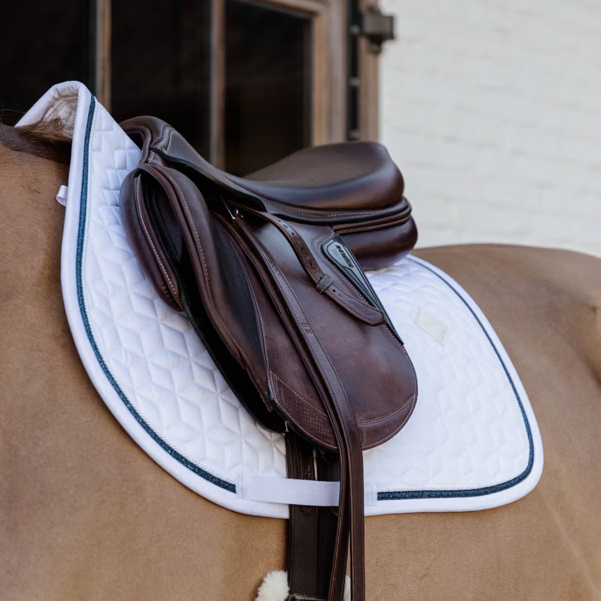 Brown saddle with a white saddle pad on a chestnut horse